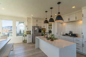 Kitchen with gas cooktop, decorative backsplash, stainless steel fridge with ice dispenser, hanging light fixtures, and an island with sink