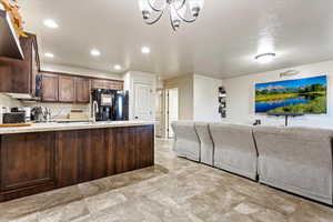 Kitchen featuring brown cabinets, a textured ceiling, a chandelier, black fridge with ice dispenser, and sink