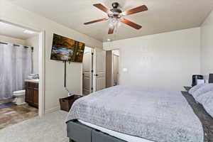 Carpeted bedroom with a textured ceiling, connected bathroom, and ceiling fan