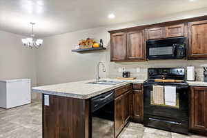 Kitchen with a notable chandelier, black appliances, sink, and kitchen peninsula