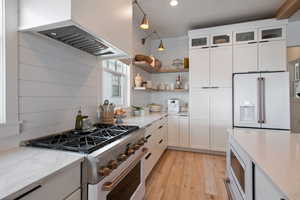 Kitchen with extractor fan, high quality appliances, light stone countertops, pendant lighting, and white cabinetry