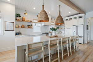 Kitchen featuring high end white fridge, a kitchen island, light hardwood / wood-style floors, pendant lighting, and white cabinets