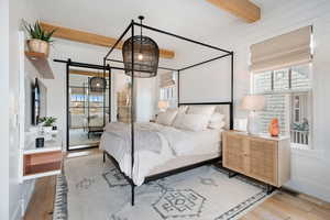 Bedroom featuring beamed ceiling, multiple windows, light wood-type flooring, and a barn door