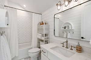 Full bathroom with vanity, shower / tub combo, toilet, and wooden walls