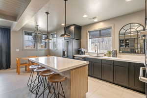 Kitchen with sink, a kitchen island, stainless steel fridge, pendant lighting, and light tile patterned floors