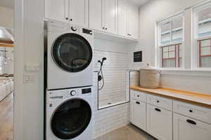 Laundry room featuring stacked washer / dryer, light tile patterned flooring, and cabinets