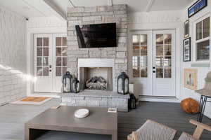 Living room with beamed ceiling, french doors, a stone fireplace, and hardwood / wood-style flooring