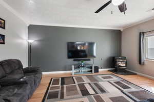 Living room featuring ornamental molding, a wood stove, hardwood / wood-style floors, and ceiling fan