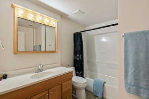 Full bathroom featuring a textured ceiling, toilet, tile patterned floors, shower / bath combo with shower curtain, and vanity