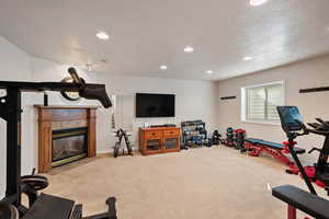 Exercise room featuring a premium fireplace, light carpet, and a textured ceiling