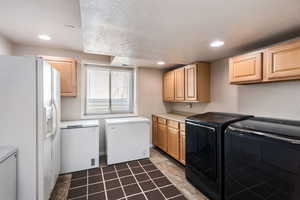 Clothes washing area featuring a textured ceiling, cabinets, and washer and clothes dryer