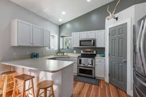 Kitchen with a breakfast bar area, kitchen peninsula, stainless steel appliances, light wood-type flooring, and white cabinets