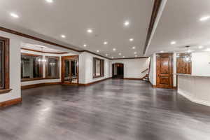 Unfurnished living room with dark wood-type flooring, crown molding, and a chandelier