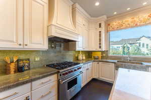 Kitchen with luxury range, dark stone counters, sink, custom exhaust hood, and tasteful backsplash