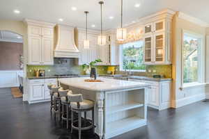 Kitchen featuring hanging light fixtures, dark hardwood / wood-style flooring, a kitchen island, premium range hood, and sink