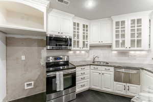 Kitchen with appliances with stainless steel finishes, white cabinets, light stone counters, and sink