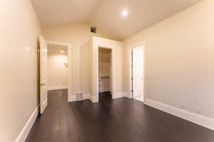 Unfurnished bedroom with a spacious closet, a closet, lofted ceiling, and dark hardwood / wood-style floors