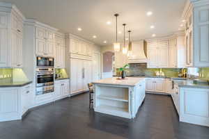 Kitchen featuring a kitchen island, dark hardwood / wood-style flooring, decorative light fixtures, built in appliances, and premium range hood