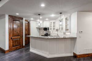 Kitchen with dark wood-type flooring, appliances with stainless steel finishes, pendant lighting, and white cabinetry