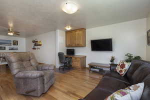 Living room featuring a textured ceiling, light wood-type flooring, and ceiling fan