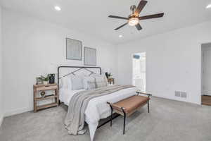 Bedroom with ceiling fan, light carpet, and ensuite bath