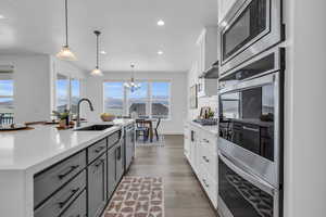 Kitchen featuring appliances with stainless steel finishes, hanging light fixtures, white cabinetry, light hardwood / wood-style flooring, and a center island with sink