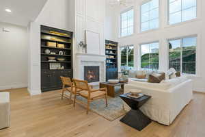 Living room with a chandelier, light wood-type flooring, a high ceiling, and a premium fireplace