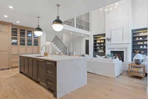 Kitchen featuring light stone countertops, sink, decorative light fixtures, a center island with sink, and light wood-type flooring