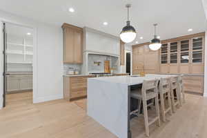 Kitchen with sink, an island with sink, light brown cabinetry, tasteful backsplash, and light hardwood / wood-style floors