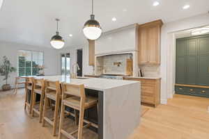 Kitchen featuring backsplash, sink, light wood-type flooring, an island with sink, and light brown cabinetry