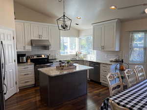 Kitchen featuring lofted ceiling, hanging light fixtures, dark hardwood / wood-style floors, stainless steel appliances, and a center island