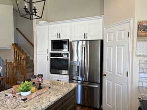 Kitchen featuring dark hardwood / wood-style floors, white cabinets, an inviting chandelier, appliances with stainless steel finishes, and light stone counters