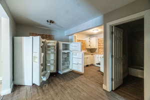 Kitchen with white cabinetry, white fridge with ice dispenser, wood-type flooring, and a textured ceiling