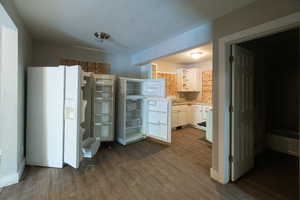 Kitchen with a textured ceiling, white cabinets, white refrigerator with ice dispenser, and hardwood / wood-style flooring