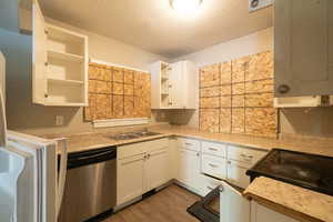 Kitchen with white cabinetry, a textured ceiling, stainless steel dishwasher, light hardwood / wood-style floors, and sink