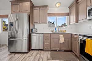 Kitchen featuring appliances with stainless steel finishes, sink, light wood-type flooring, and light stone counters