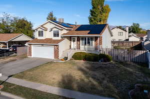 View of front of home featuring central AC unit, a garage, solar panels, and a porch