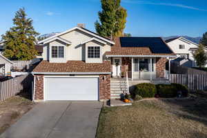 Split level home featuring a porch, solar panels, a front lawn, a mountain view, and a garage