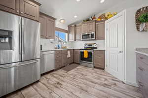 Kitchen with vaulted ceiling, appliances with stainless steel finishes, light stone counters, and light wood-type flooring