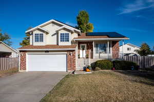 Tri-level home with covered porch, a front yard, a garage, and solar panels