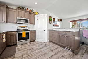 Kitchen with light stone countertops, lofted ceiling, appliances with stainless steel finishes, and light hardwood / wood-style floors