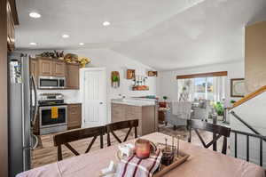 Kitchen featuring lofted ceiling, stainless steel appliances, light stone countertops, light wood-type flooring, and a textured ceiling