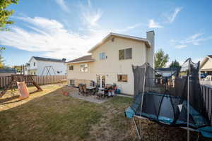 Back of property with a yard, a trampoline, a patio area, and a playground