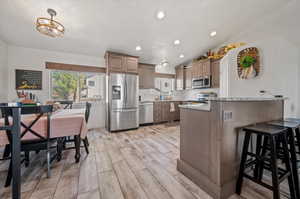 Kitchen featuring light stone counters, a breakfast bar area, vaulted ceiling, light hardwood / wood-style floors, and stainless steel appliances