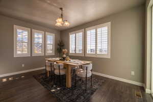 Dining room featuring a wealth of natural light, dark wood-type flooring, a textured ceiling, and an inviting chandelier