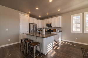 Kitchen with a breakfast bar, a kitchen island with sink, dark wood-type flooring, white cabinets, and stainless steel appliances