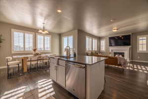 Kitchen featuring dark hardwood / wood-style flooring, decorative light fixtures, dishwasher, a chandelier, and an island with sink