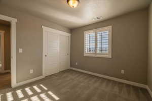 Unfurnished bedroom featuring carpet flooring, a textured ceiling, and a closet