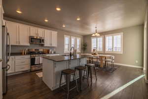 Kitchen with white cabinets, a healthy amount of sunlight, an island with sink, and stainless steel appliances