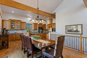 Dining area featuring an inviting chandelier, high vaulted ceiling, beamed ceiling, light hardwood / wood-style floors, and sink